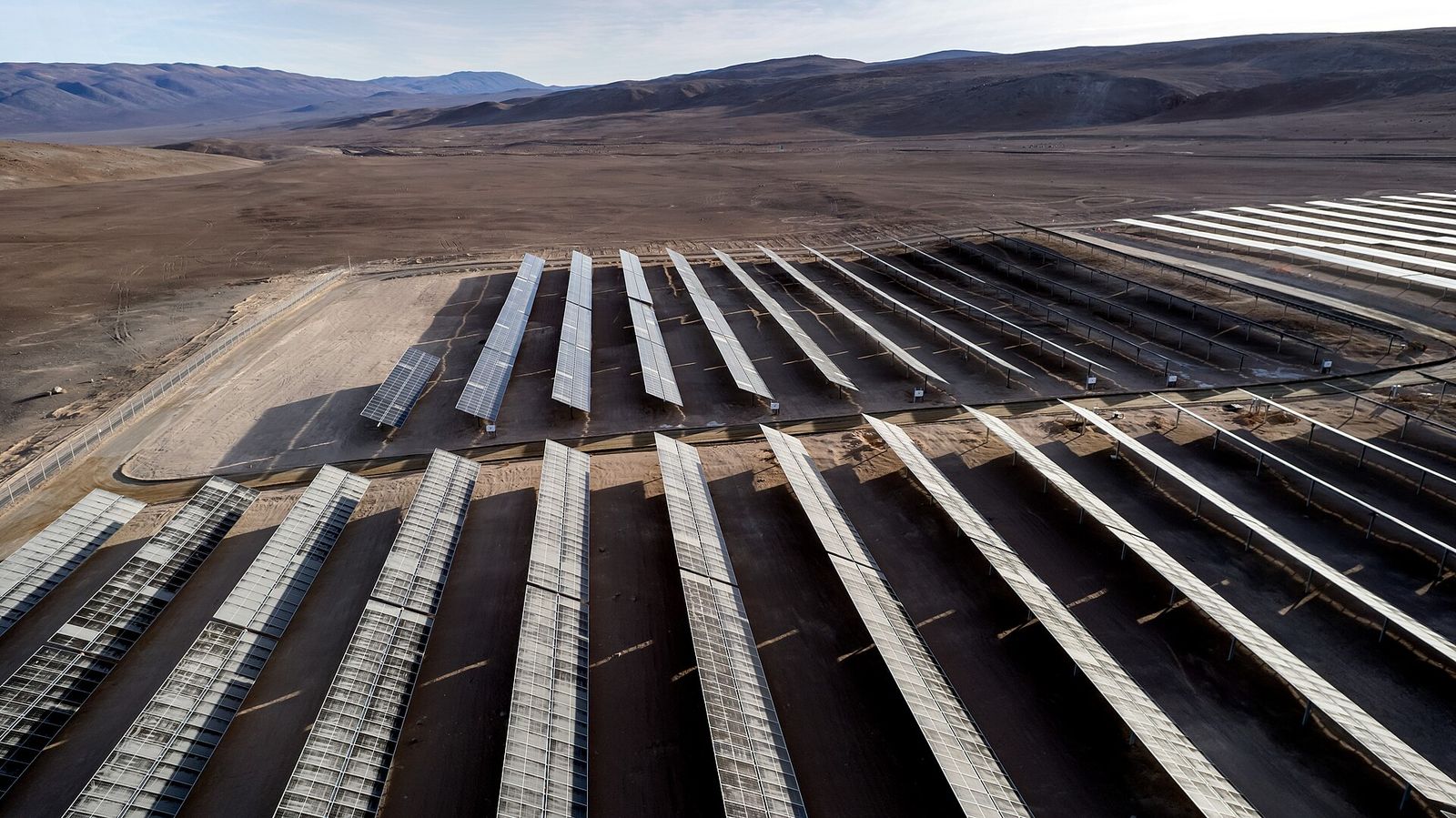 Hileras de paneles solares sobre seguidores en la planta Paranal-Armazones, con el suelo del desierto de Atacama y cerros al fondo