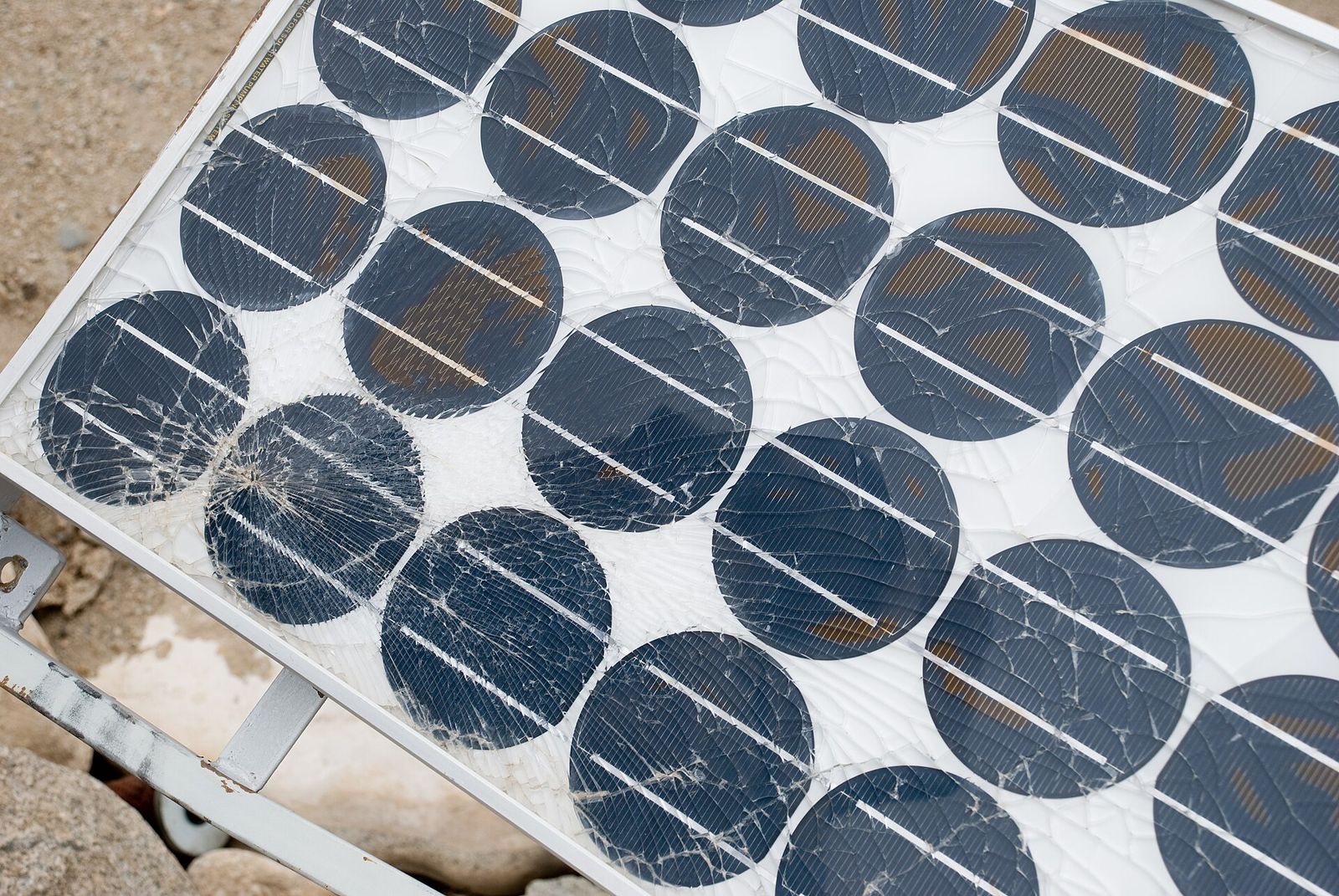 Primer plano de un panel solar antiguo de celdas redondas, con el vidrio frontal trizado en múltiples grietas y manchas de color café en las celdas