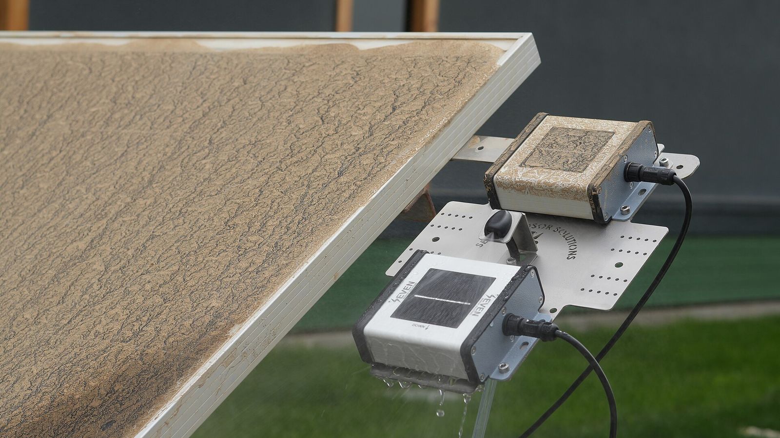 Sensor automático de ensuciamiento montado en el borde de un panel solar cubierto de polvo: una unidad de referencia sucia y otra limpia de la que escurre agua